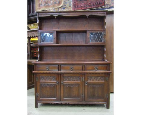 An old charm oak cottage dresser in the old English style, the base enclosed by three linen fold panelled doors beneath three