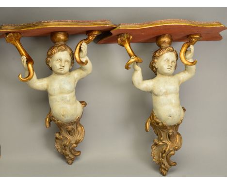 A PAIR OF LATE 19TH/EARLY 20TH CENTURY GILDED AND PAINTED WOODEN PUTTI SUPPORT WALL SHELVES, the serpentine shaped shelf rest