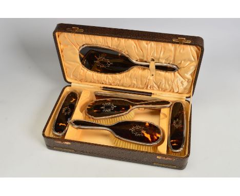 A CASED GEORGE V SILVER AND TORTOISESHELL PIQUE WORK DRESSING TABLE SET, comprising hand mirror, four brushes and a comb, mak