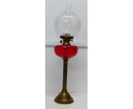 A brass oil lamp with red glass reservoir