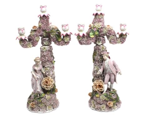 A pair of late 19th century German three arm candlestick figures: a gentleman and his lady companion standing amidst mass flo