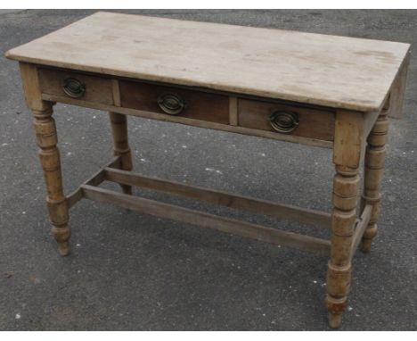 A late 19thC stripped pine kitchen table, with one drop leaf, three frieze drawers with plate back handles and cylindrical su