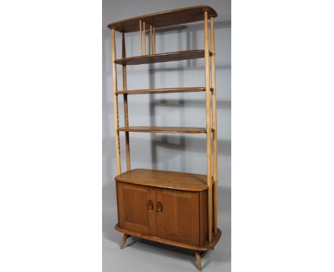 An Ercol light wood shelf unit, with oblong shelves broken by cylindrical columns above double cupboard on cylindrical suppor
