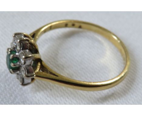 A cluster dress ring with a central green stone surrounded by eight small white stones which do not test positive for diamond