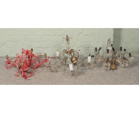 A heavy red cast metal electrical chandelier light fixture along with one glass chandeliers and one in plastic, also with ele
