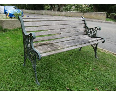 A two seat garden bench with weathered slatted seat raised on decorative pierced cast iron end supports, 124 cm wide 