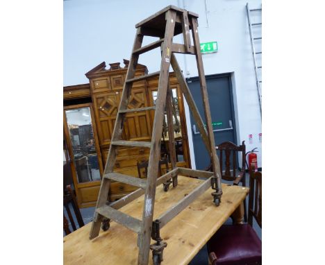 A SLINGSBY PINE LADDER SLOPING TO A RIGHT ANGLE SUPPORT WITH IRON WHEELS AT THE BASE SPRUNG SO THAT THE WEIGHT OF THE USER PU