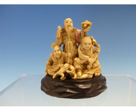 MITSUTAMA, AN IVORY OKIMONO OF GAMA SENNIN STANDING HOLDING A SCROLL AND A MINOGAME WHILE SINGING, THE TWO MEN SEATED BELOW E