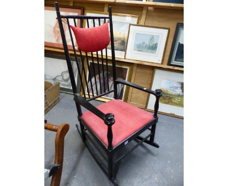 AN EBONISED WOOD ROCKING CHAIR. RED SEAT, DISC KNOPPED HAND RESTS TO THE STRAP ARMS.