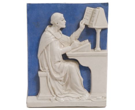 A BLUE AND WHITE POTTERY PLAQUE in the style of Della Robbia, depicting a monk copying text at a desk 32cm wide x 40.5cm high