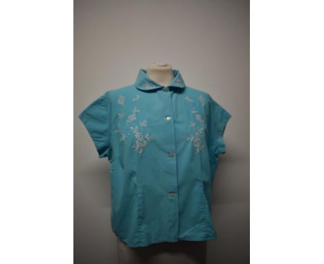 A 1950s blue blouse, having white embroidery, cap sleeves and button to front, medium size.
