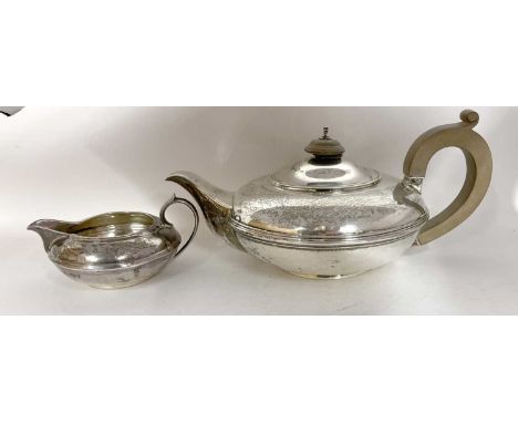 A George V silver teapot and cream jug of compressed circular form with reeded detail, the teapot engraved with a crest and p