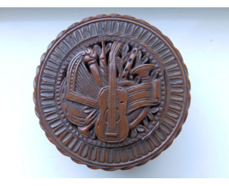 A 19thC French coquilla nut patch box, of circular plan with threaded cover decorated with a musical trophy, 2” diameter.