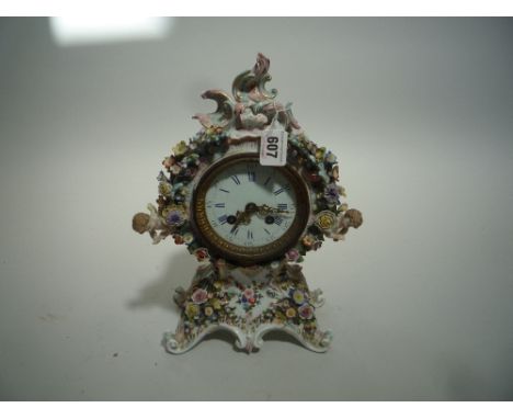 A CONTINENTAL FLORALLY ENCRUSTED PORCELAIN MANTEL CLOCK, rococo style case mounted with cherubs, height 32cm (key and pendulu