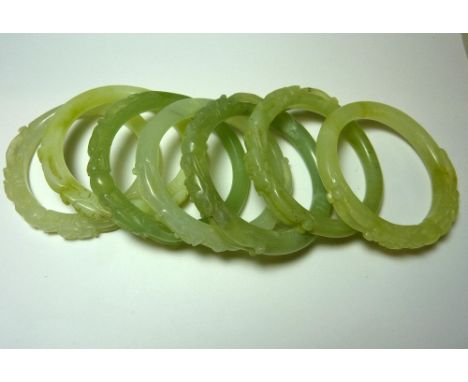 A COLLECTION OF CARVED JADEITE BANGLES, each with a carved relief of a dragons face to the plain bangle (7)