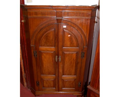 A George III mahogany freestanding corner cupboard having twin recessed panel arched doors