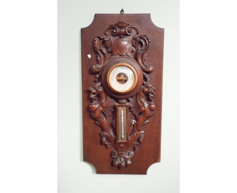 Wall barometer and thermometer in carved oak frame standing on a plaque style background