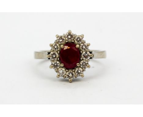 An 18ct white gold cluster ring set with an oval cut ruby surrounded by brilliant cut diamonds, (U).
