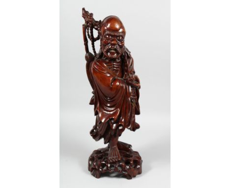 A LARGE CHINESE CARVED HARDWOOD FIGURE OF A SAGE holding a scroll, with inset teeth and eyes, the figure raised on a carved h