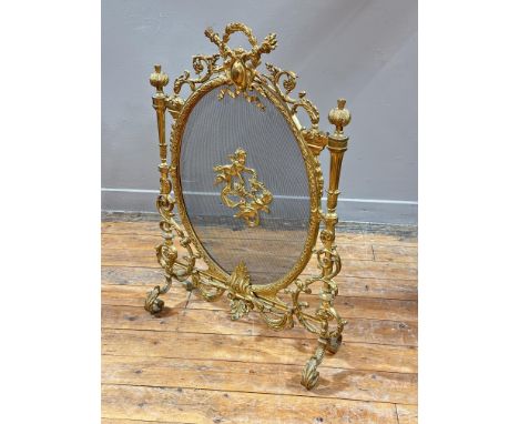 A late 19th century gilt-metal firescreen the oval mesh panel centred by a cast pair of garlanded putti within an elaborately