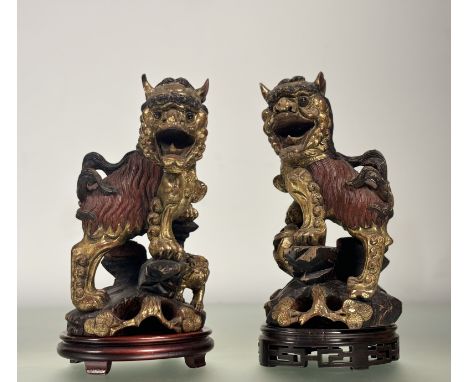 A pair of decorative Chinese carved giltwood Buddhist lions, in characteristic poses, highlighted in red and black, on associ
