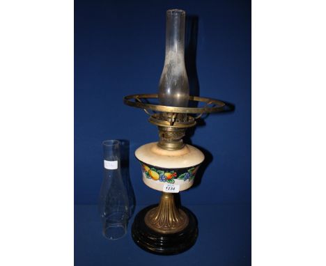 An Oil Lamp with brass column and reservoir painted with fruits, with clear glass chimney but no shade and standing on a blac