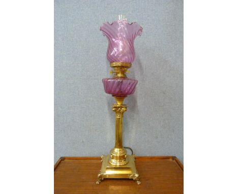 A Corinthian column brass oil lamp, with cranberry glass oil reservoir and shade 