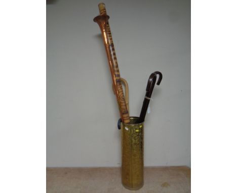 A brass embossed stick stand containing assorted walking sticks, copper and brass horn, didgeridoo  