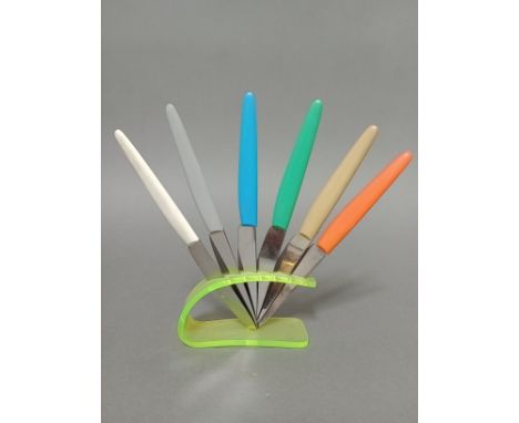 A vintage neon green knife rest with set of multi-coloured handled knives, the steel blades marked 'Rostfrei'. 