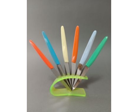 A vintage neon green knife rest with set of multi-coloured handled knives, the steel blades marked 'Rostfrei'. 