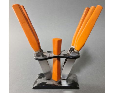 An Art Deco bakelite knife stand with a set of six orange bakelite handled knives, the serrated blades marked 'PAHL' and 'Ros