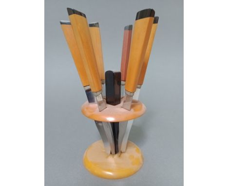 An Art Deco black and butterscotch bakelite knife stand of circular form with six knives, the steel blades marked 'Rostfrei'.