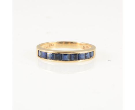 A sapphire half eternity ring, nine square cut stones channel set in an all yellow metal mount, 3.4mm wide at front, shank ma