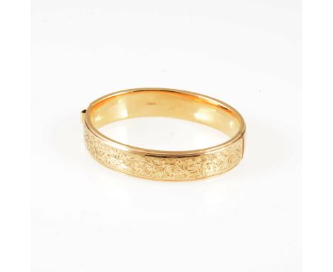 A 9 carat yellow gold 12mm wide hollow half hinged bangle, scroll decoration to front, approximate weight 17.3gms.