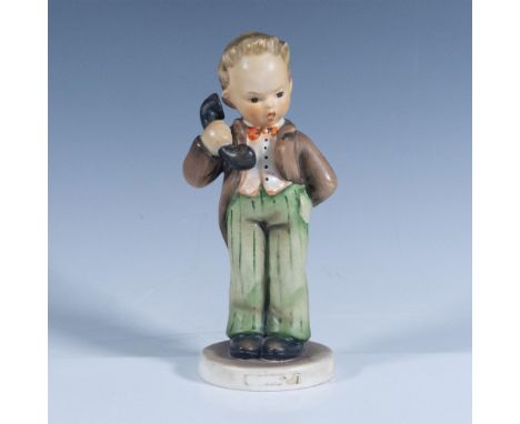 A ceramic figurine featuring a boy answering a phone call, dressed in a brown jacket and pants, a red bowtie, and a white shi