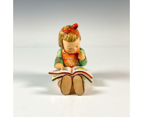A matte hand painted figure of a young girl reading a picture book. M.I. Hummel impressed. Goebel backstamp. Artist: M.I. Hum