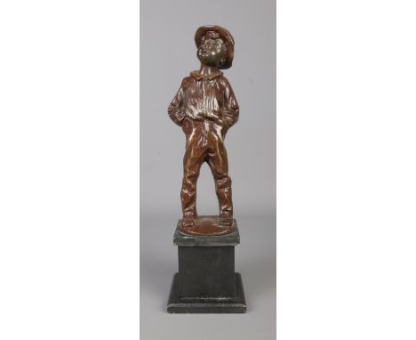 A bronze sculpture of a young boy raised on a square slate plinth. Modelled smoking a cigar, stood with his hands in his pock