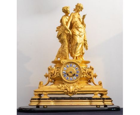 A Louis XVI revival large ormolu gilded table clock under glass dome, depicting two young ladies holding hands casting and gi