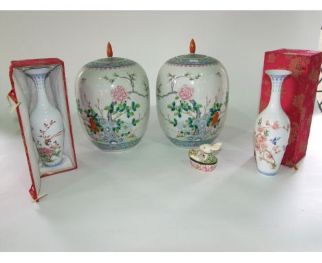 A pair of oriental white ground vases and covers of ovoid form with Famille Rose flowering, tree and rock decoration with red