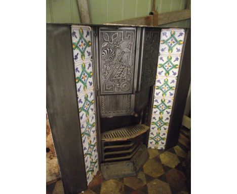 A reclaimed asthetic period cast iron fire insert/grate with decorative relief panels flanked by tiled friezes, together with