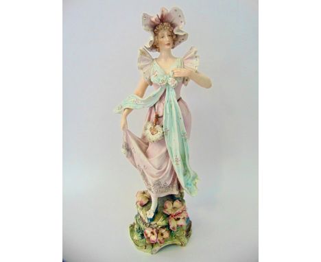 A large late 19th century continental model of a female character in bonnet and pink dress raised on a floral encrusted base 