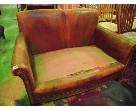 An early 20th century two seat sofa, worn tan leather upholstered with rolled arms and moulded feet (lacks seat cushions)