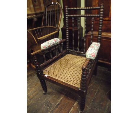 An Arts & Crafts bobbin moulded elbow chair with cane panelled seat and upholstered arm panel