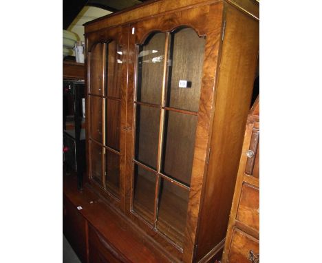 A small reproduction walnut and figured walnut veneered bookcase enclosed by a pair of segmented and arched glazed panelled d