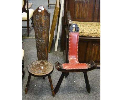 An early 20th century hardwood spinning stool, profusely carved; another with leather padding, shaped seat , tripod legs (2)