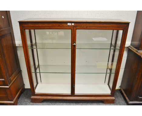 An early 20th century oak glazed bookcase, enclosing three shelves, bracket feet