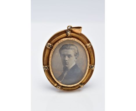 A YELLOW METAL PORTRAIT PENDANT, of an oval form, holding a photo of a gentleman, within a textured collet mount, within a fu