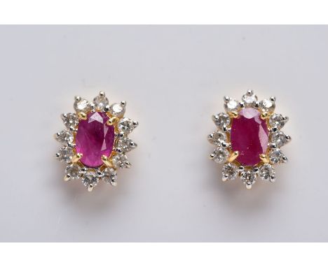 A PAIR OF 18CT GOLD RUBY AND DIAMOND CLUSTER EARRINGS, each designed with a central claw set, oval cut ruby, within a round b