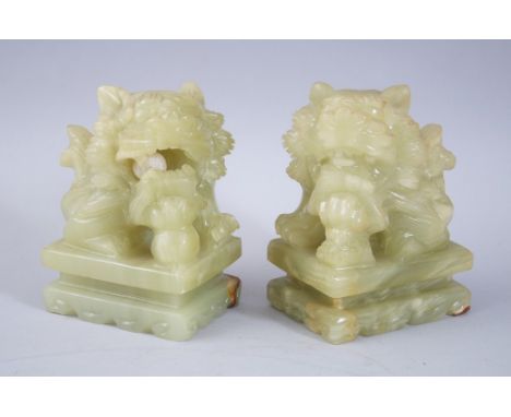 A PAIR OF 20TH CENTURY CHINESE JADE / JADELIKE HARDSTONE LION DOGS,  both sat upon carved pedestal bases with their paws upon