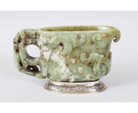 A CHINESE 18TH CENTURY CARVED JADE LIBATION CUP, the sides carved with animals and scrolls, on a silver base. 14cms long.
